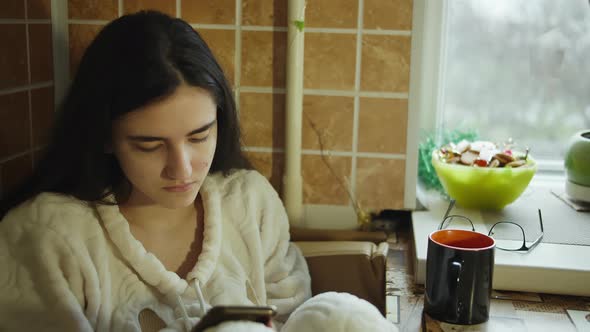 Brunette girl cozy sitting in the kitchen with a mobile phone, camera tracking alt