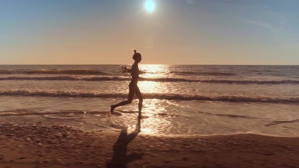 A slender woman runs and jumps on the waves of sea water on a sandy beach. alt