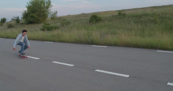 Young Happy Boy Skateboarding on a Road with Lines Out of City in Summer Time alt