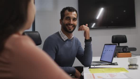 Middle eastern man smiling while looking at his female colleague in meeting room at office alt