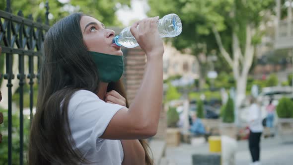 Woman With Protective Mask Drinking Water On Street