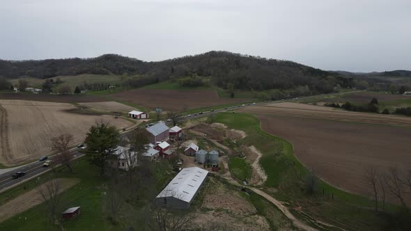 View of farm in valley with highway running past the buildings. Mountains on each side.