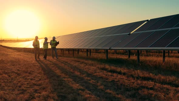 Three Solar Energy Specialists Walking Through a Solar Park at Sunset alt