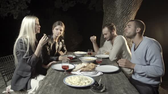 Group of Four Happy Men and Women Friends Smile and Enjoy Aperitif in Outdoor Rural Scenic at Night alt
