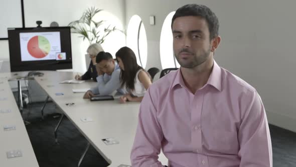 MS Man sitting with arms crossed while people working in background