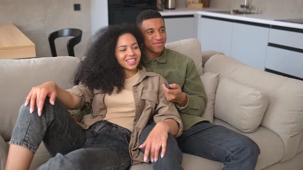 Young AfricanAmerican Couple in Love Sitting at the Sofa and Watching TV