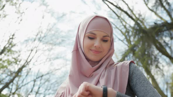 Pleasant Woman in Hijab Looking at Smart Tracker for Checking Jogging Distance alt