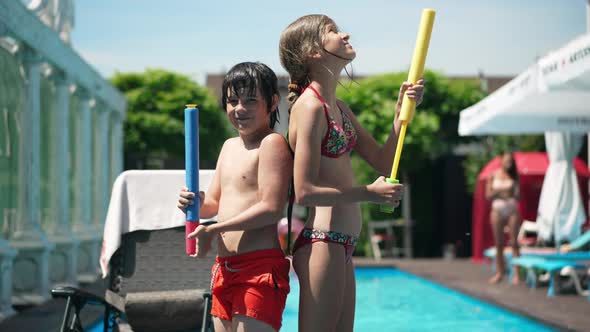 Side View of Confident Caucasian Children Standing at Swimming Pool with Water Gun Back to Back and alt