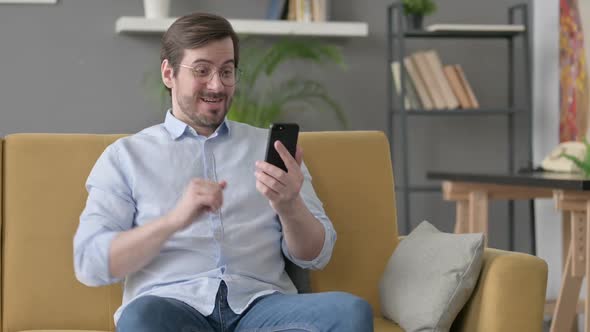 Young Man Having Success on Smartphone at Home alt