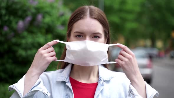 A young, attractive girl on the street puts on a protective mask alt