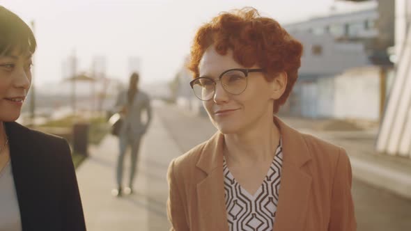 Asian and Caucasian Businesswomen Walking Outdoors and Talking alt