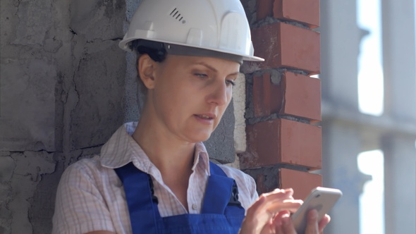 A young construction female worker sits at a site and works