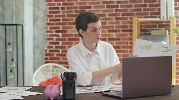 Businesswoman with Short Hair and a White Shirt Irritably Speaks Via Video Link on a Laptop Showing alt