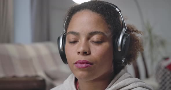Gorgeous African American Young Woman in Headphones Opening Eyes Winking Looking at Camera alt