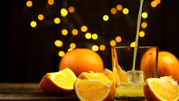 A Few Slices And A Whole Orange And Juice Are Poured Into A Glass With Lights In The Background