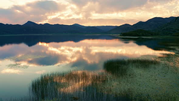 Beautiful sunset sky reflected in lake - marsh grass and silhouettes of mountains alt