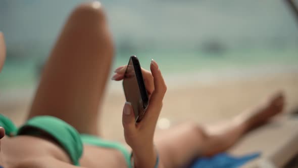 Woman In Bikini Relaxing On Beach. Woman Looking Mobile. Tourist Girl Playing In Game Smartphone. alt