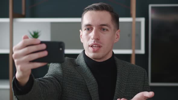 Portrait of Happy Businessman Making Facetime Video Calling with Smartphone at Modern Office Waving