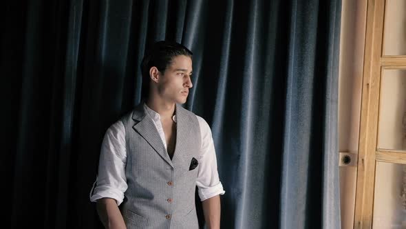Attractive young fashion man in a suit posing on a background of blue curtains. alt