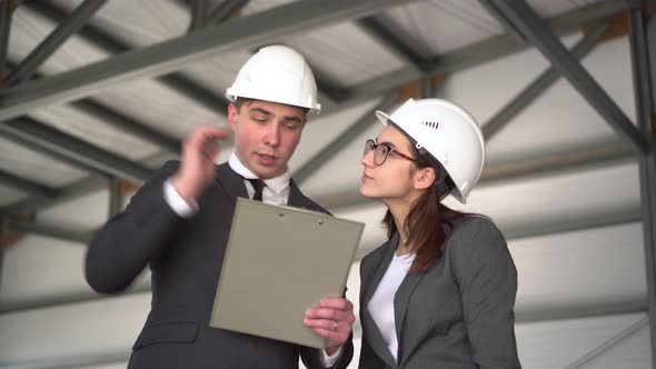 Woman Approves the Project. Young Man and Woman in Helmets with Documents at a Construction Site alt