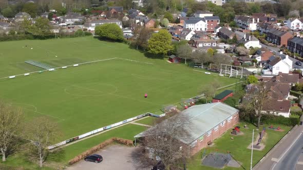 Aerial drone shot panning over village football pitch and housing estate, England alt