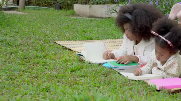 Happy African family with children lying reading or writing to book in the garden, kids go to picnic alt
