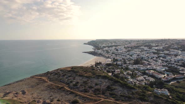 Wide revealing view over Town encircling Praia da Luz, Algarve. Aerial alt