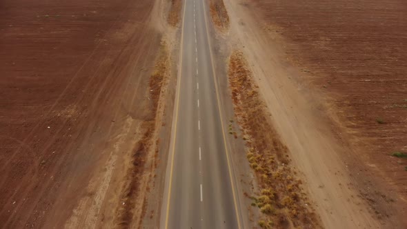drone aerial shot of the desert's empty road revealing the endless horizon and some cars. alt