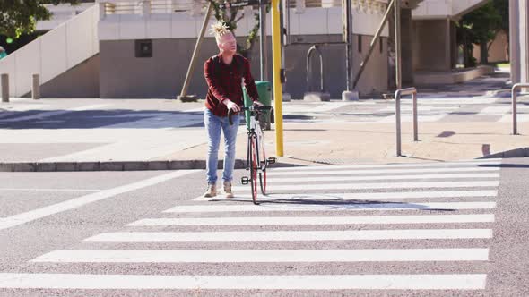 Albino african american man with dreadlocks crossing road with bike alt