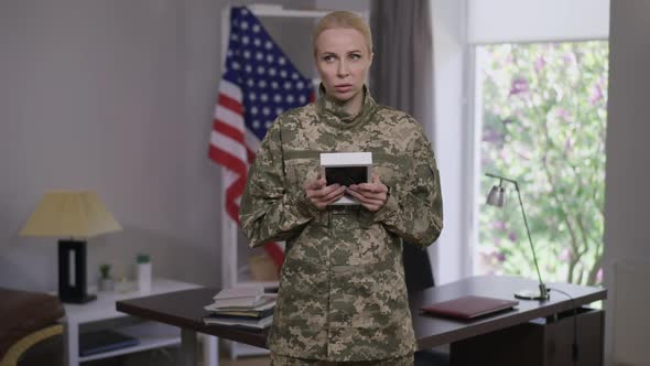 Frustrated Lonely Woman in Military Uniform Admiring Photo Frame Standing Indoors with USA Flag at alt