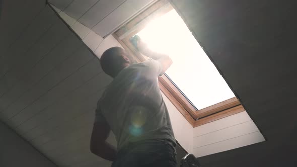 Caucasian Man Washes the Attic Window Bright Sun Illuminates the Man in the Window During the Repair