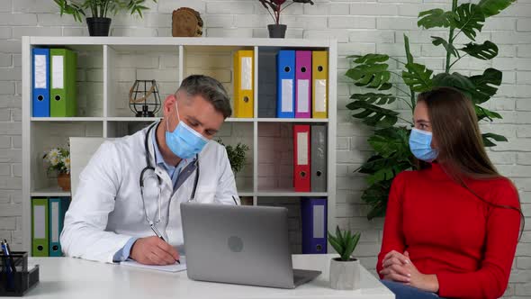 Doctor and patient wears protective masks on faces in hospital communicates alt