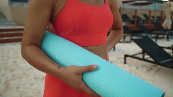 Closeup Shot of Woman Standing on the Beach with Sport Mat in Hands