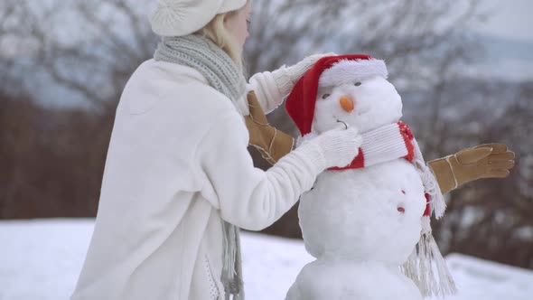 Happy Young Woman Having Fun in Winter. Snowman and Funny Girl. Make a Snow Man. alt