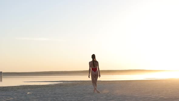 Sexy Woman in Swimsuit Walking Along Beach at Sunset