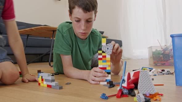 Young boy playing and constructing with toy bricks on the living room floor alt