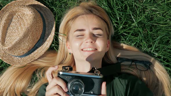 Young woman tourist lies on the grass and taking a picture on retro camera on vacation
