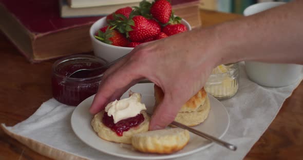 An Afternoon Tea with a Scone, Cream and Jam in Cornwall. Man Reaching for Scone with his Hand and E alt