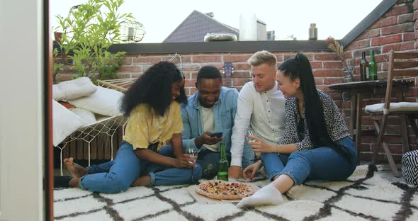 Multiethnic Friends which Sitting on the Carpet on Balcony and Using Phone alt
