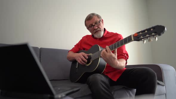 Elderly Man or Musician with Glasses and Red Shirt with Laptop Computer Learning To Play Guitar with alt
