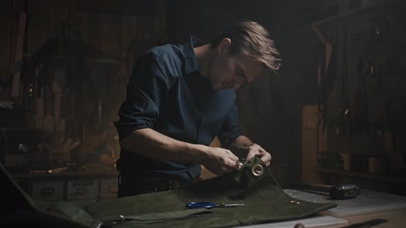 Young Focused Professional Craftsman Unpicking Canvas Fabric at Workshop Cutting Seams with Knife alt