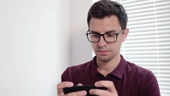 Man Sms Texting Using App on Smart Phone in the Office Standing By the Window alt