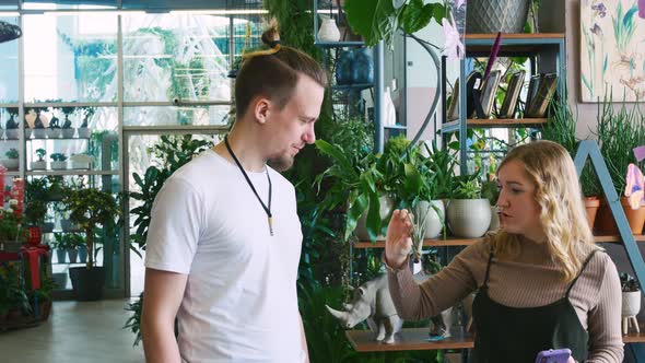 A Husband and His Wife are Smiling Choosing Houseplants in a Greenhouse Among the Greenery alt