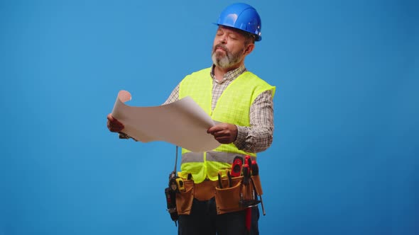 Senior Man Builder in Hardhat Looking at Blueprints Against Blue Background