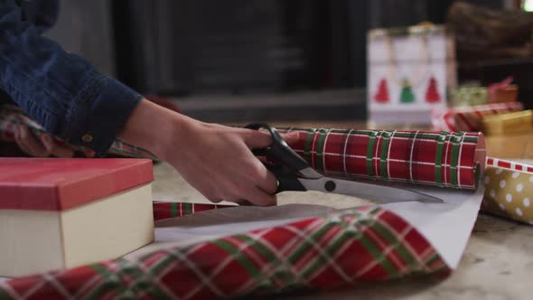 Mid section of woman cutting wrapping paper for Christmas presents at home alt