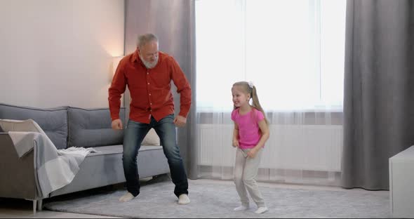 Happy Little Girl Dances with Young Father in the Middle of the Living Room