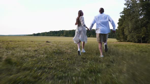 Young Couple Happy at Sunset Runs Across the Field Holding Hands