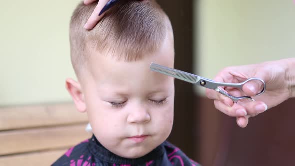 Closeup View of Front Portrait of a Little Baby Boy with Closed Eyes While Getting Haircut with alt