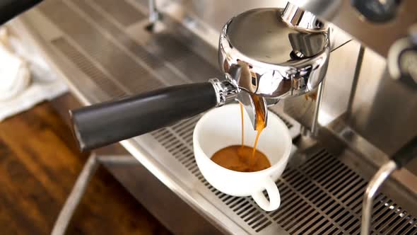 Espresso being brewed by coffee maker machine flowing through portafilter into the cup