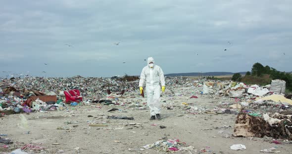 Ecologist in Protective Suit and Gas Mask Walking with Tablet Near Polluted Land alt